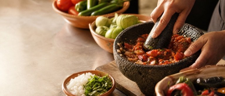 Hands grinding fresh salsa in a stone molcajete