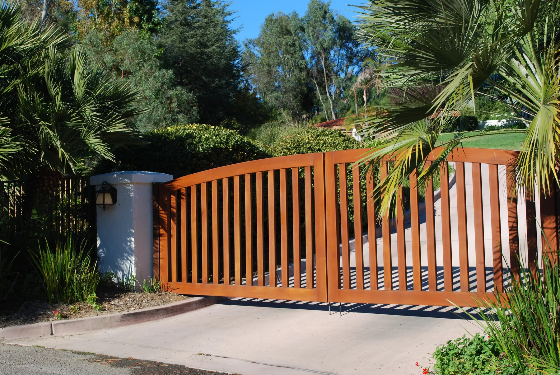 Custom cedar driveway gate framed by mature landscaping